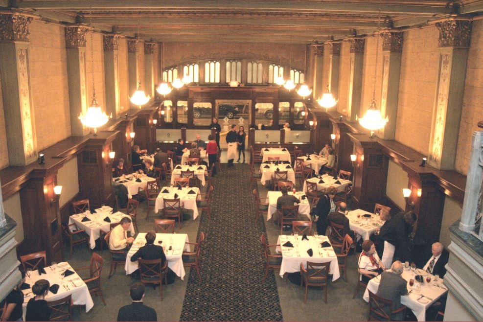 Elegant historic dining hall with ornate columns, pendant lighting, and white-clothed tables